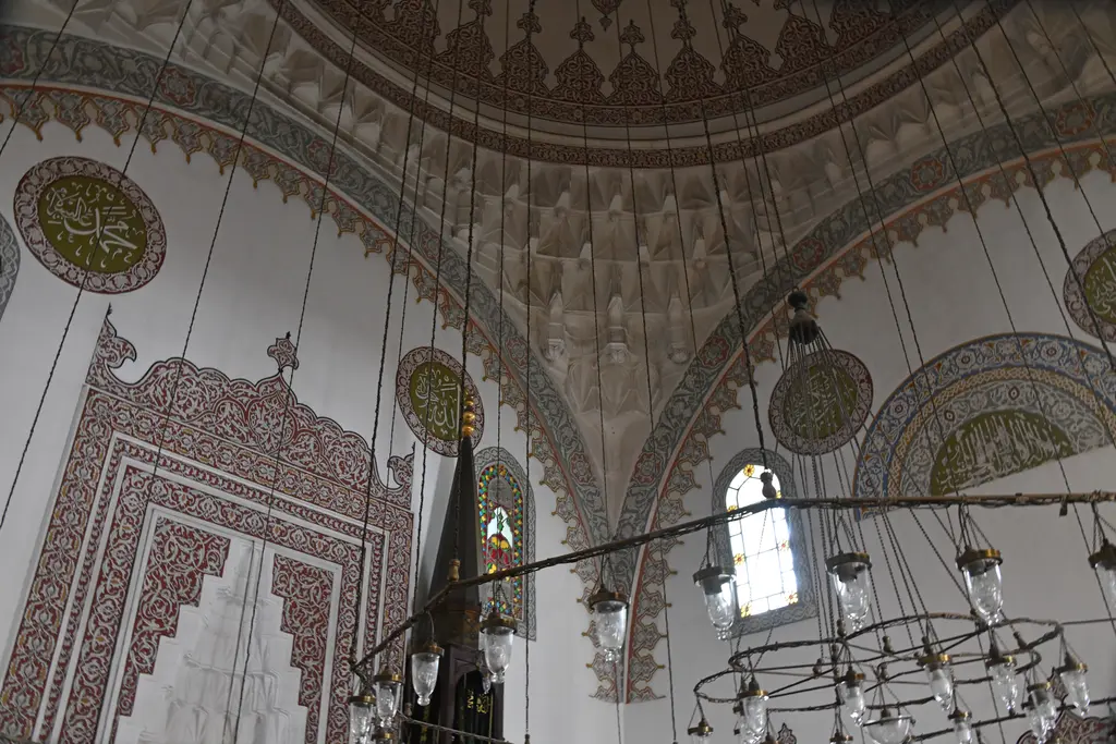 Firuz Ağa Camii'nde kubbe geçişi; kalem işi süslü kemer yüzeyleri, yazı madalyonları, pencereler ve sarkan kandil halkası.