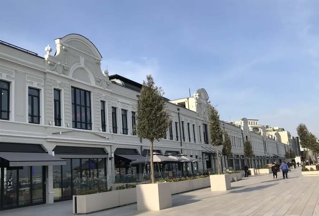 Galataport'ta Paket Postanesi; beyaz cepheli uzun tarihi bina, kemerli pencereler, önde saksılı ağaçlar ve taş kıyı yolu.
