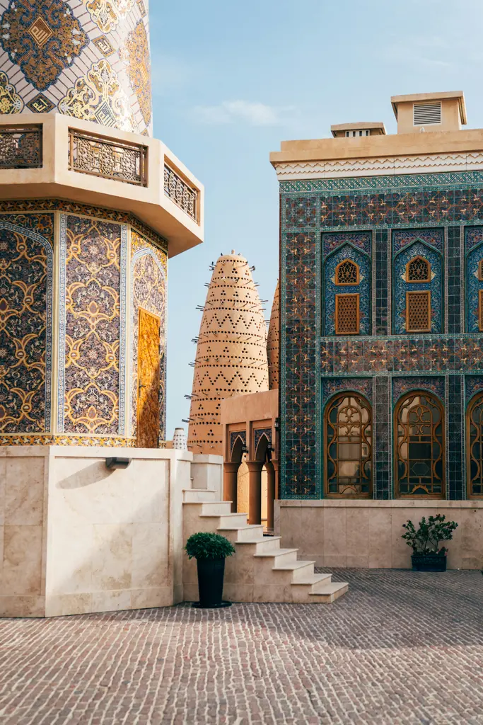 Doha'da mozaikle kaplı bir cami; mavi-mor çinilerle bezeli silindirik minare, altın rengi desenli gövdesi ve yanındaki taş merdiven.