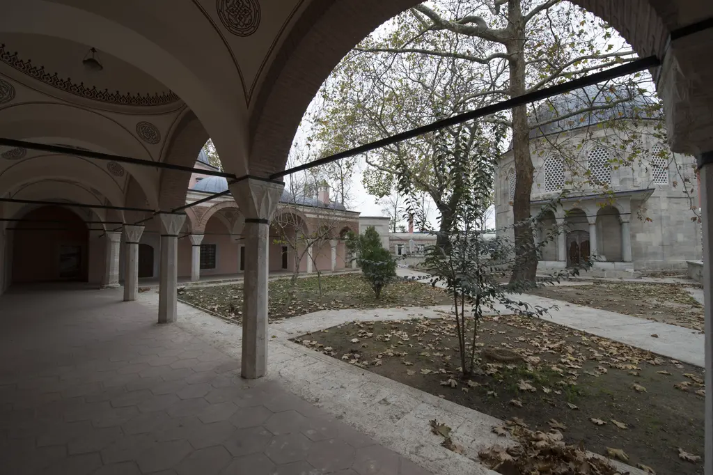 Zal Mahmud Paşa Külliyesi'nde medrese revağı; kemerler ve mermer sütunlar arasından görünen bahçe, ağaçlar ve sağda türbe.
