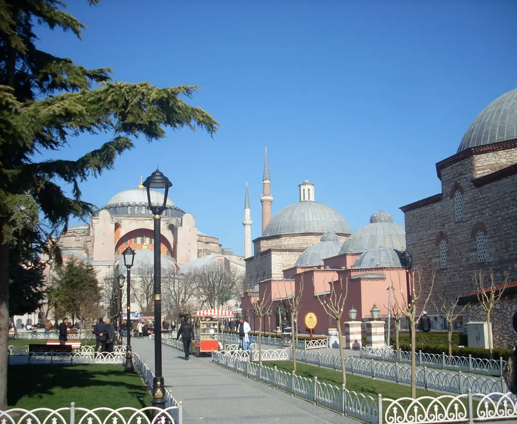 Yaya yolundan bakış; solda Ayasofya'nın kubbesi ve minareleri, sağda hamamın pembe duvarıyla kubbeleri, ortada ağaçlar.