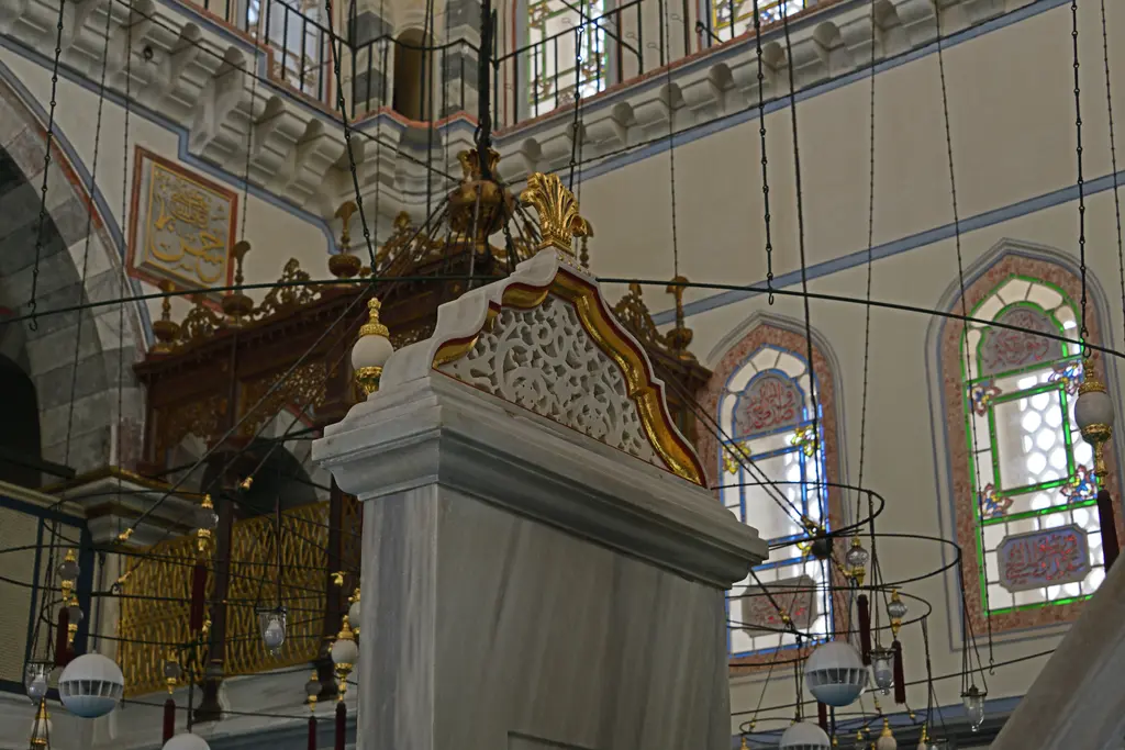 Ayazma Camii'nde mermer kürsü; önde beyaz mermer gövde, arkada yaldızlı ahşap mahfil ve renkli camlı pencereler.