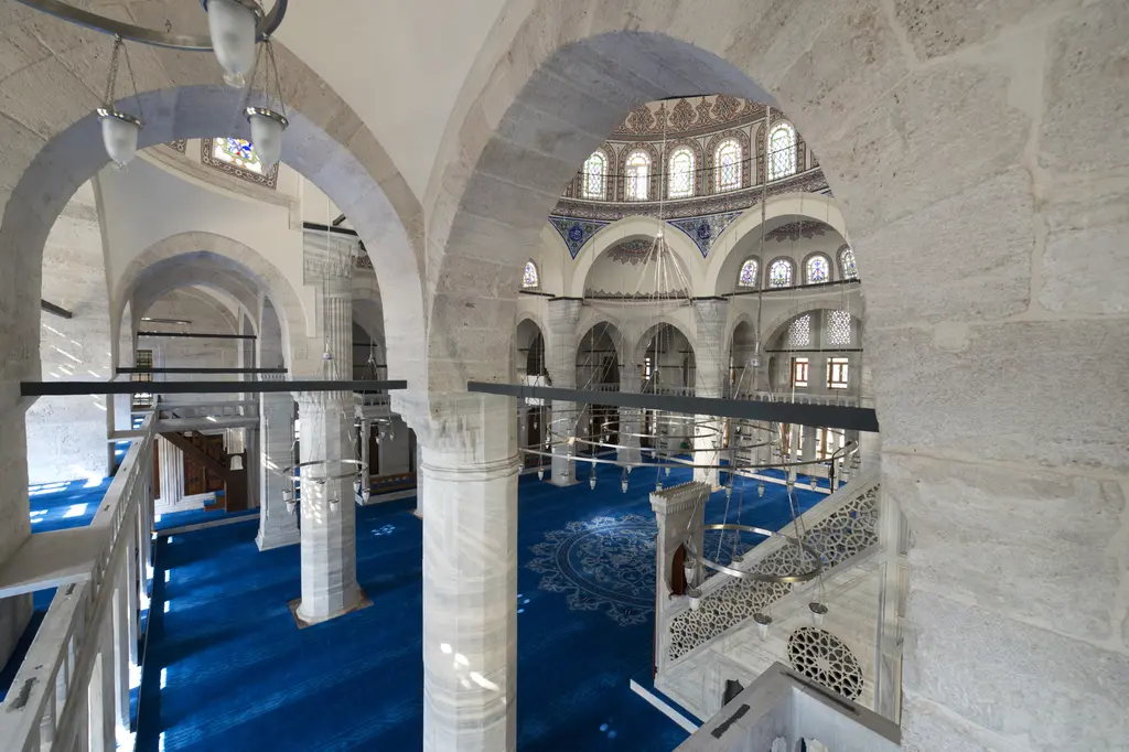 Azapkapı Sokullu Mehmed Paşa Camii'nde payeler; beyaz taş ayaklar ve kemerler, arasında mahfil merdiveni, mavi halı ve uzakta kubbe.