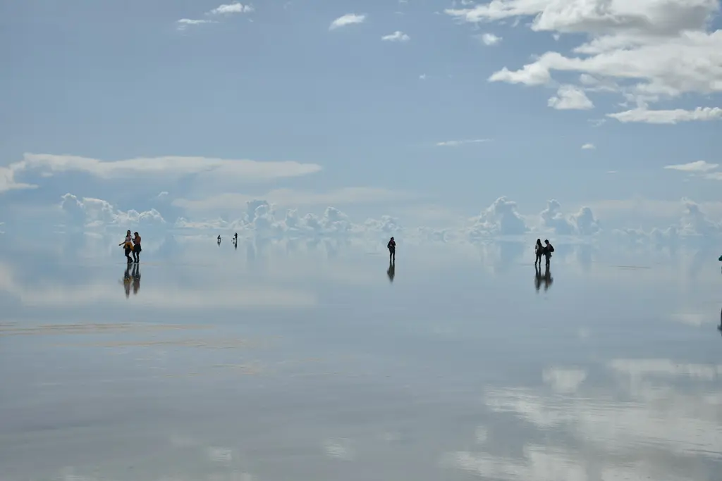 Bolivya'da Uyuni Tuz Gölü; ince su tabakasının gökyüzünü ayna gibi yansıttığı uçsuz bucaksız beyaz düzlükte silüet halinde duran ziyaretçiler.