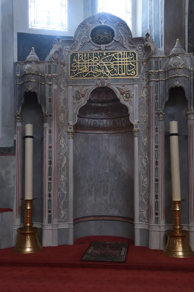 Zeyrek Camii'nin mihrabı; kemerli mermer niş, iki yanında uzun pirinç şamdanlar, üstte hat yazılı pano ve altta kırmızı halı.