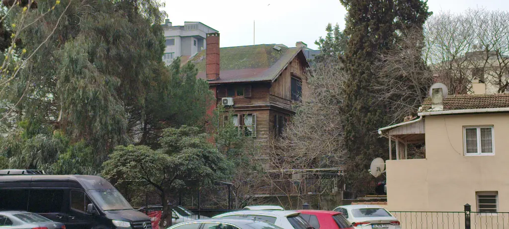 Göztepe'de Tütüncü Mehmet Efendi Caddesi'nde köşk; ağaçların ardında tuğla bacalı ahşap yapı ve önde park alanı.