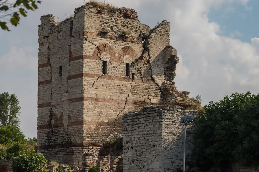 Bir kulenin çatlamış gövdesi yakından; kesme taş sıraları arasında kırmızı tuğla bantları, gövdeyi boydan boya yaran derin çatlak.