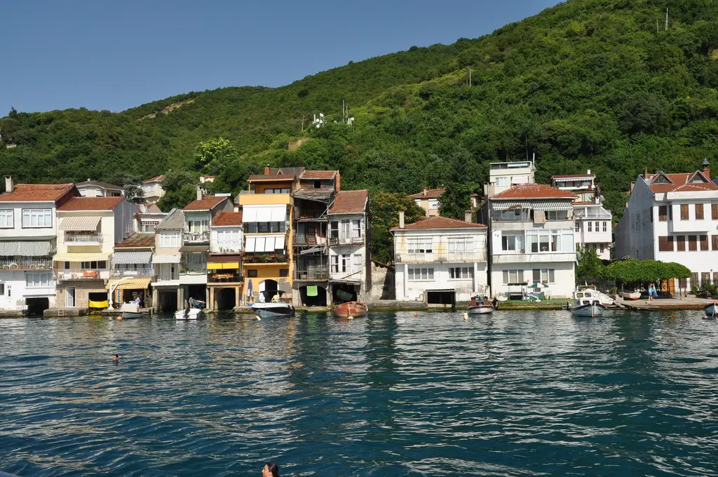 Anadolu Kavağı'nda Boğaz kıyısında yan yana dizilen evler; kiremit çatılar, suya açılan kapılar ve arkada yeşil tepe.