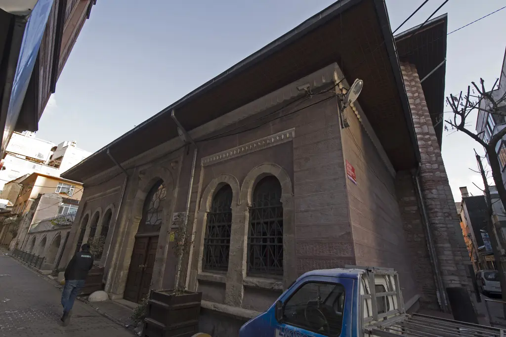 Arap Camii'nin yan cephesi; tuğla ve taş duvarda sivri kemerli büyük pencereler, önde dar sokak ve park etmiş araç.