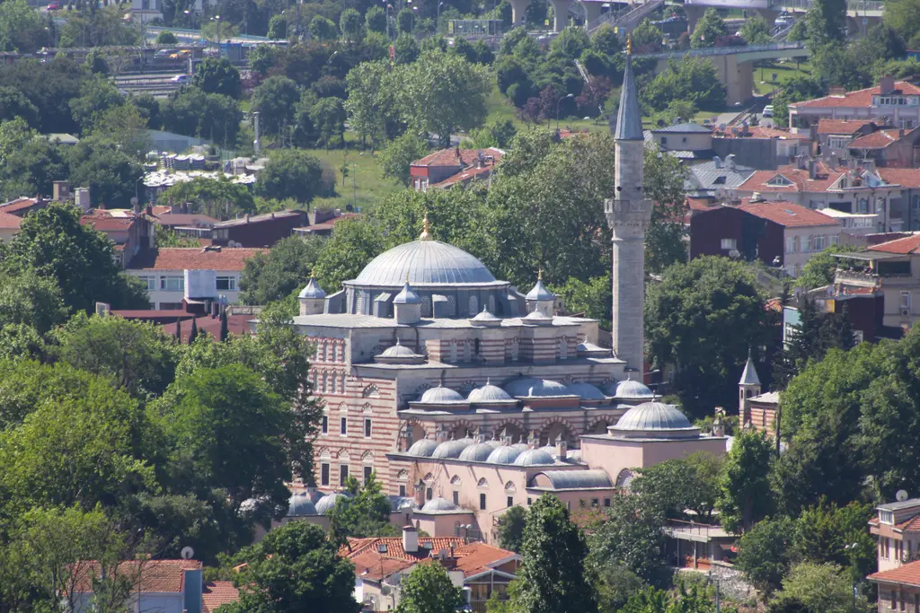 Eyüpsultan'da Zal Mahmud Paşa Camii'nin uzaktan görünümü; kurşun kubbe, minare, medrese kubbeleri ve çevresinde ağaçlarla kırmızı çatılı evler.