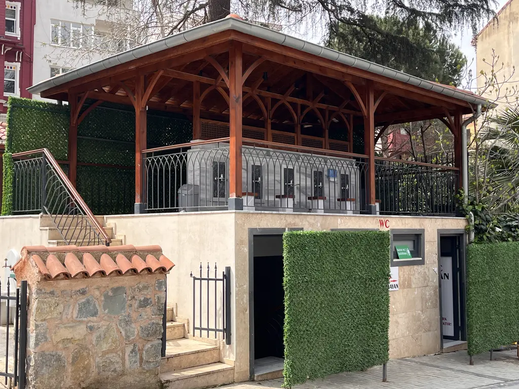 Şeyh Nevruz Camii'nin bahçesinde ahşap çatılı yapı; oymalı korkuluk, taş kaide ve kiremit kaplı bahçe duvarı.