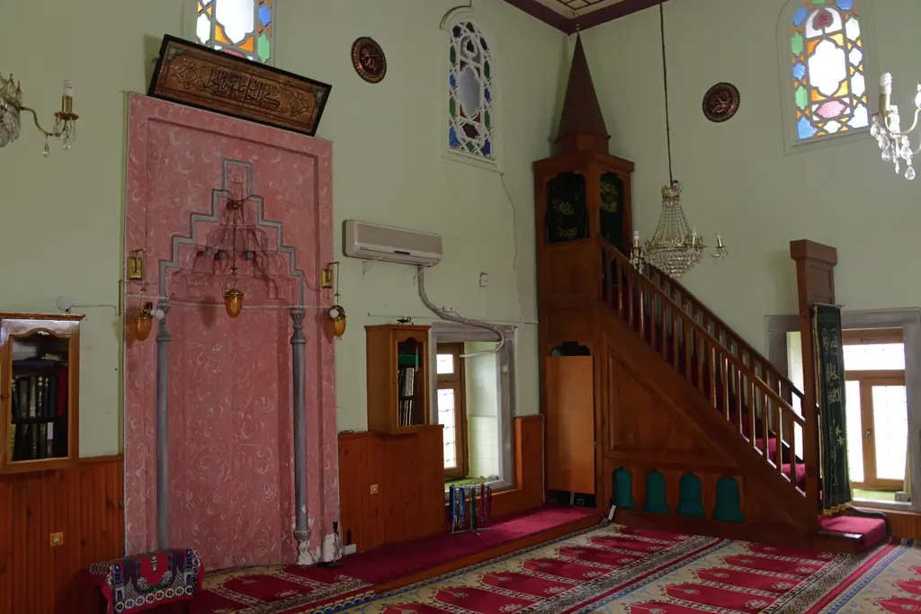 Defterdar Camii'nin kıble duvarı; pembe mermer mihrap, ahşap minber, renkli camlı üst pencereler ve kristal avizeler.