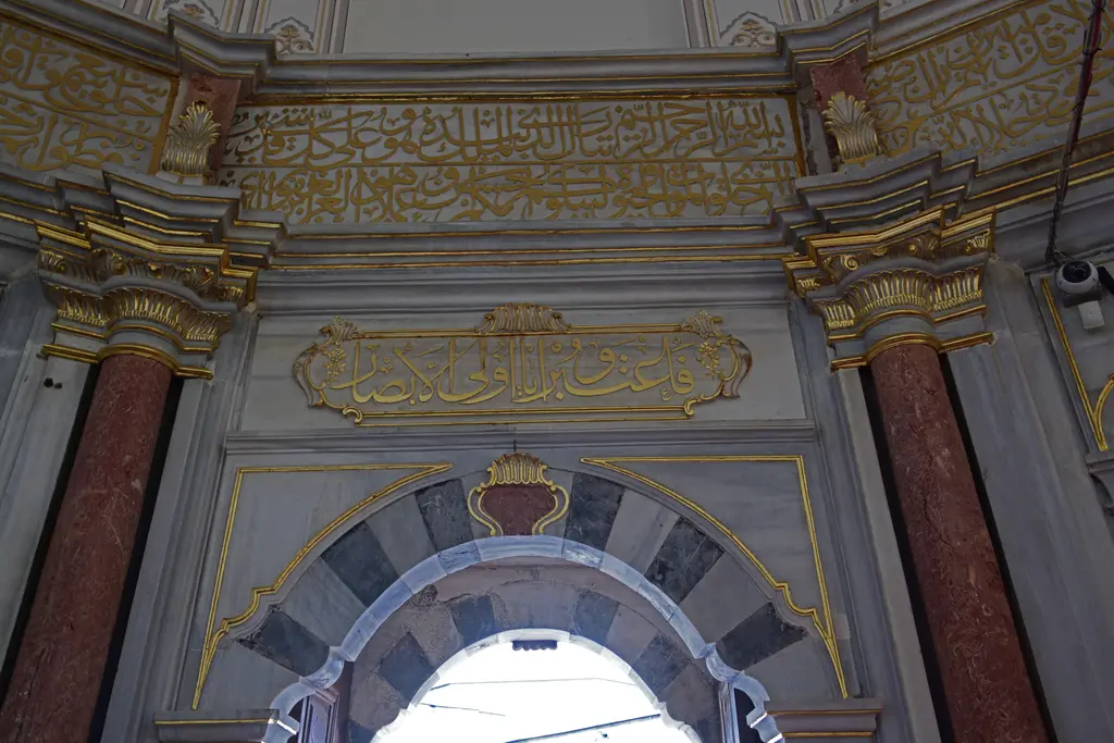 Mihrişah Valide Sultan Türbesi'nin içi; giriş kemeri, siyah-beyaz mermer söveler, yaldızlı yazı kuşakları ve pembe mermer sütunlar.