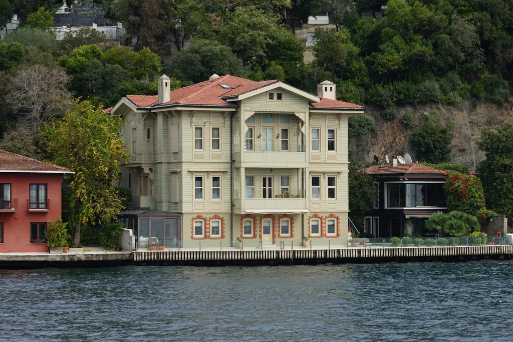 Hacı Ahmet Bey Yalısı; krem renkli üç katlı cephe, kiremit çatı, yanında kırmızı ev ve önde rıhtım.
