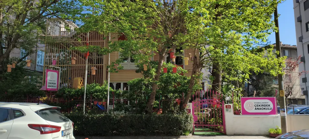 Göztepe'de Karanfil Sokak'ta konak; yeşil ağaçların ardında ahşap yapı, pembe tabelalı anaokulu kapısı ve bahçe.