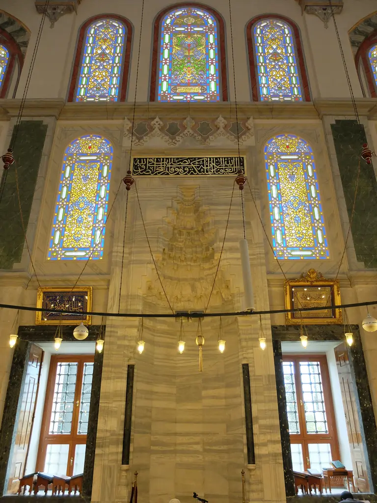 Fatih Camii'nin mihrabı; bal rengi mermer pano içinde mukarnas kavsaralı niş, iki yanda koyu yeşil sütunceler, üstte altın hatlı siyah kitabe ve renkli camlı yüksek pencereler.