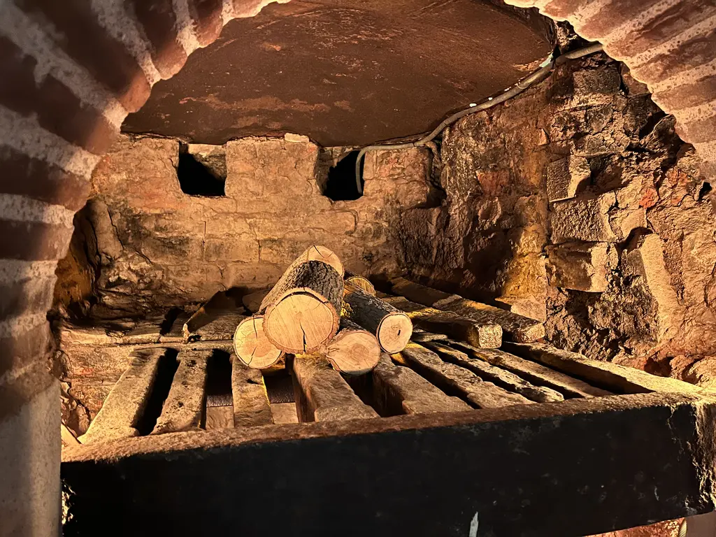 Çinili Hamam'ın külhanı; tuğla tonozun altında ocak ağzı, demir ızgara üzerinde kesilmiş kütükler ve arkada cehennemlik açıklıkları.