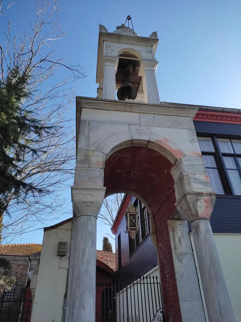 Aya Yorgi'nin kemerli girişi; mermer çan kulesinin altında kırmızı tonozlu geçit ve ardında avlu.