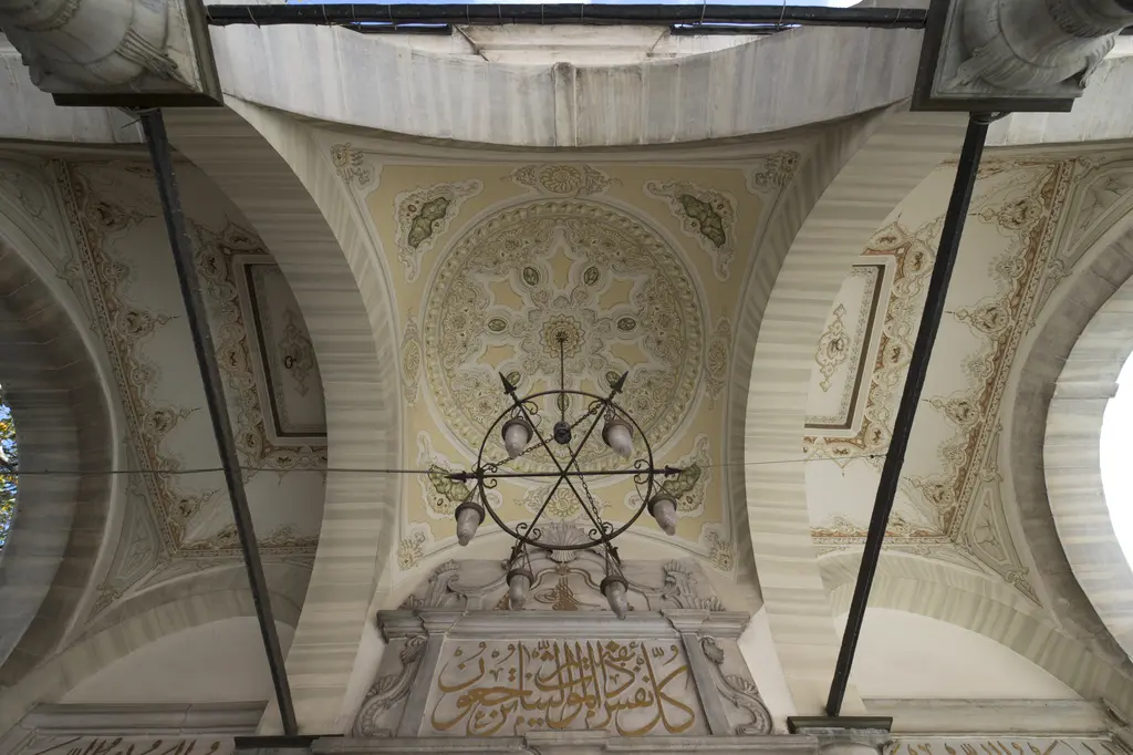 Şah Sultan Türbesi'nin revak tavanı; kemerler, kalem işi çiçek motifleri, kandil askısı ve kapı üstündeki yazı panosu.