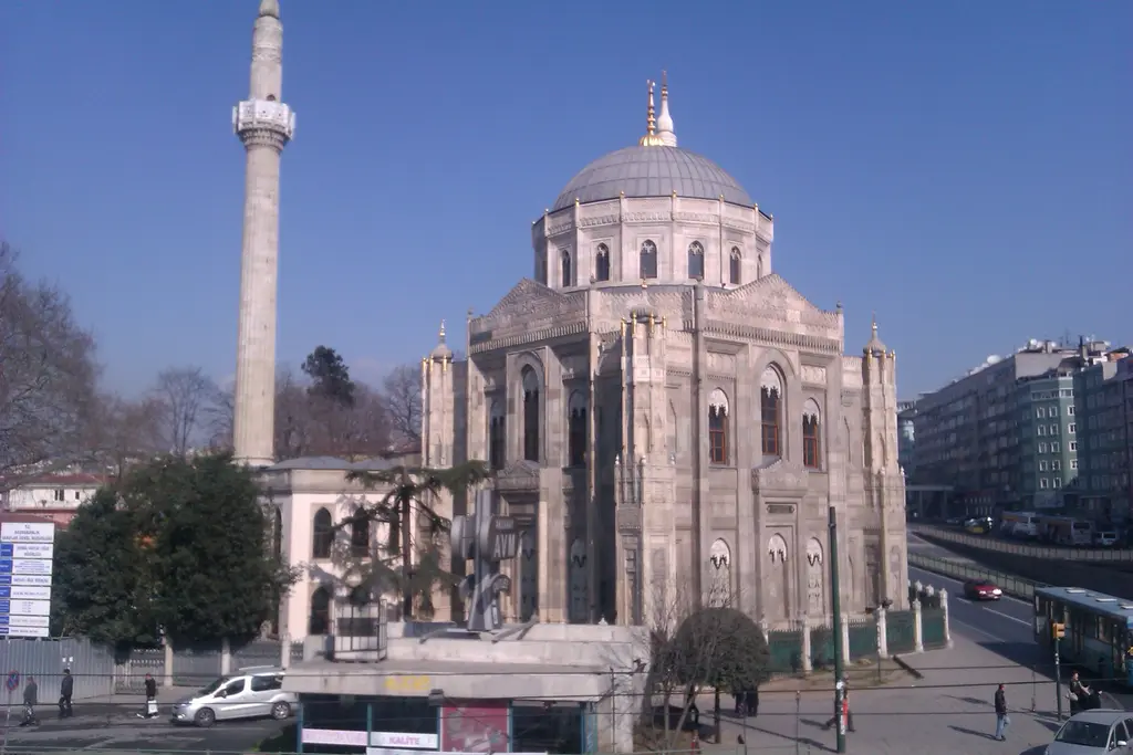 Pertevniyal Valide Sultan Camii; pembe tonlu taş cephe, gotik pencereler, minare, önde ağaçlar ve Atatürk Bulvarı'ndaki trafik.