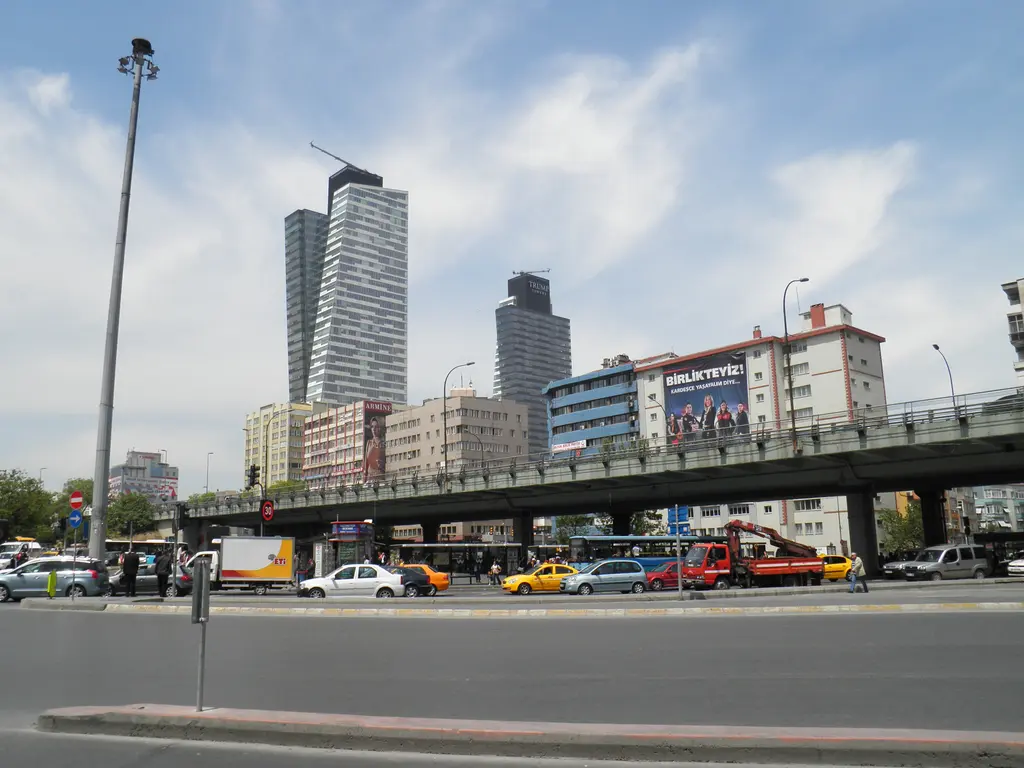Mecidiyeköy'de Büyükdere Caddesi; köprülü kavşak, sarı taksiler ve otobüsler, arkada inşaatı süren iki gökdelen.