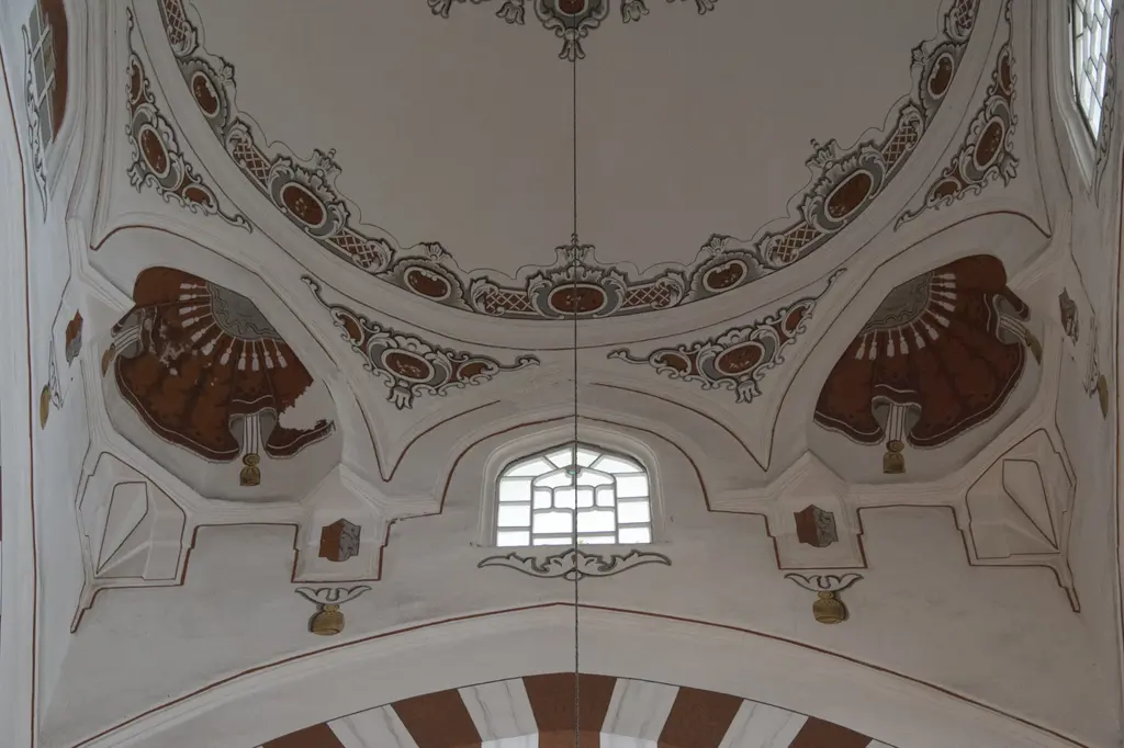 Şehzade Camii'nde pandantif bezemesi; kiremit kırmızısı tonlarda boyanmış yelpaze biçimli mukarnas motifleri, aralarında kemerli bir pencere ve beyaz sıva.