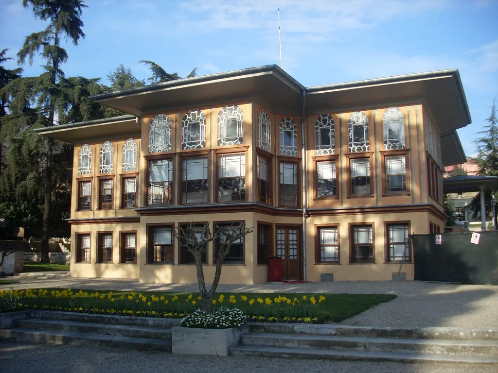 Aynalıkavak Kasrı'nın Haliç'e bakan cephesi; iki katlı sarı yapı, kahverengi pencere çerçeveleri, önünde çiçekli tarh ve basamaklar.