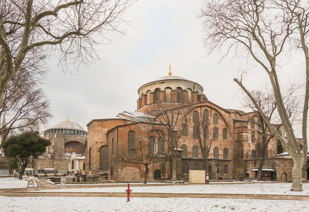 Aya İrini kar altında; önde karla kaplı bahçe ve çıplak ağaçlar, ortada kilisenin kubbesi, solda Ayasofya'nın kubbesi ile minareleri.