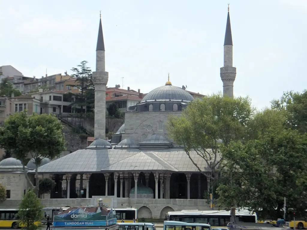 Üsküdar meydanından Mihrimah Sultan Camii; kubbe, iki minare, önde ahşap çatılı son cemaat yeri ve meydanda yürüyenler.
