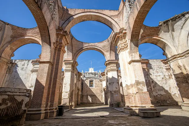 Antigua Guatemala'da depremde yıkılan sömürge dönemi katedralinin kalıntıları; tuğla kemerler ve dökülmüş sıvalı sütunlar arasından görünen berrak mavi gökyüzü.