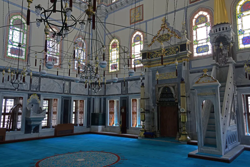 Ayazma Camii'nin harimi; mavi halı, avizeler, renkli camlı pencereler, sağda minber ve mermer kürsü.