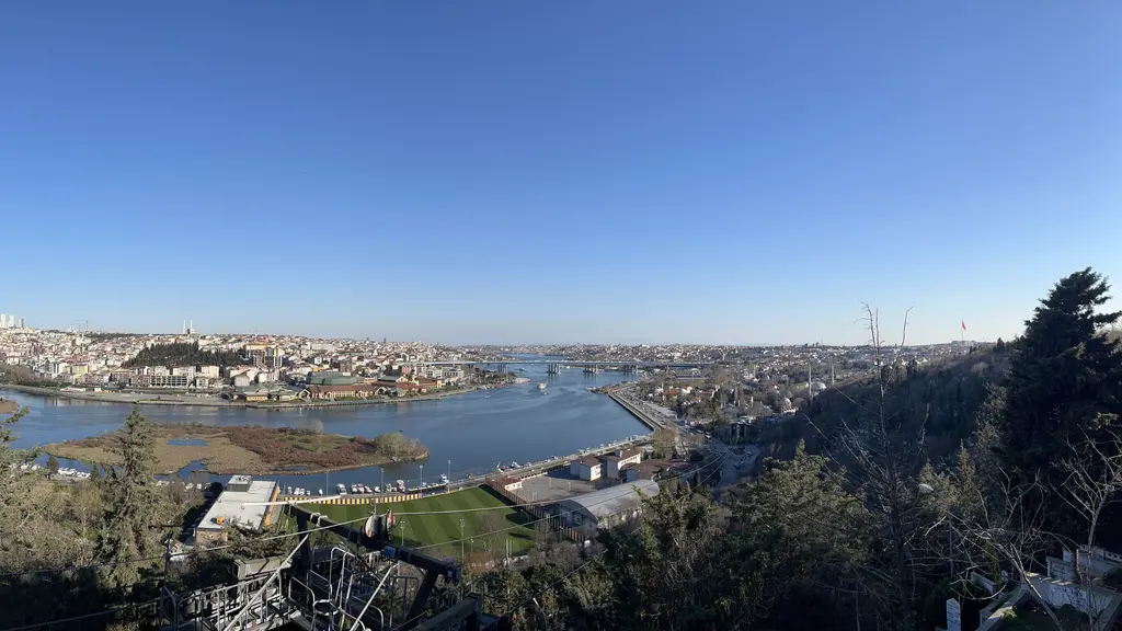 Pierre Loti Tepesi'nden Haliç panoraması; açık mavi gökyüzü, kıyıdaki semtler, adacıklar ve sağda yamaçtaki ağaçlar.