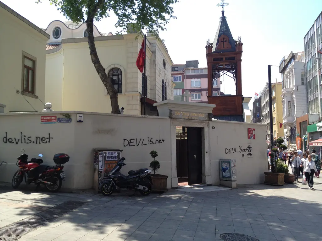 Kadıköy'de Surp Takavor Kilisesi; sokak boyunca avlu duvarı, kilise cephesi, çan kulesi ve park etmiş motosikletler.