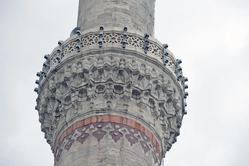 Yavuz Sultan Selim Camii'nde minare şerefesi; mukarnas dolgulu konsollar, taş korkuluk, gövdedeki kırmızı taş bant ve üstte peteğin başlangıcı.