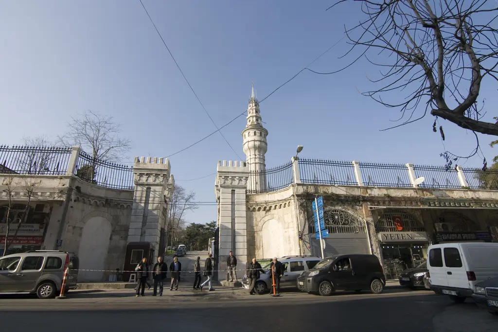Kampüs kapısı ve Beyazıt Kulesi; sokakta yayalar ile araçlar, duvarın ardındaki ağaçlar ve arkada kulenin üst bölümü.