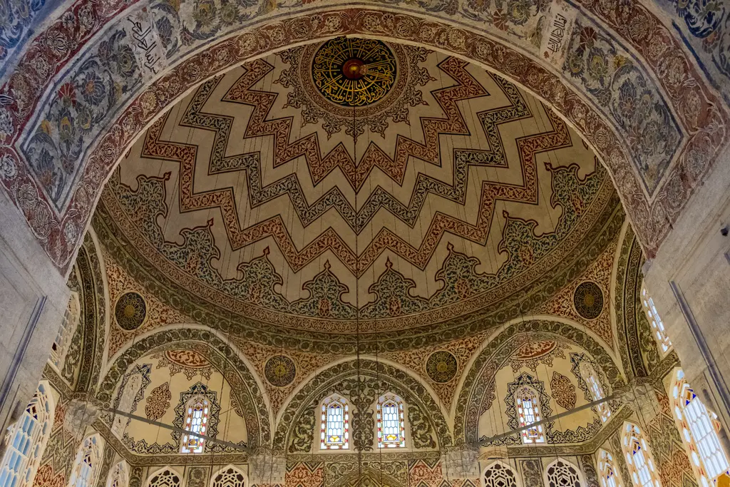 Sultan Ahmed Türbesi'nin kubbesine içeriden bakış; zikzaklı kalem işi kuşaklar, ortada göbek, kemerli pencereler ve çini kaplı köşe tromplar.