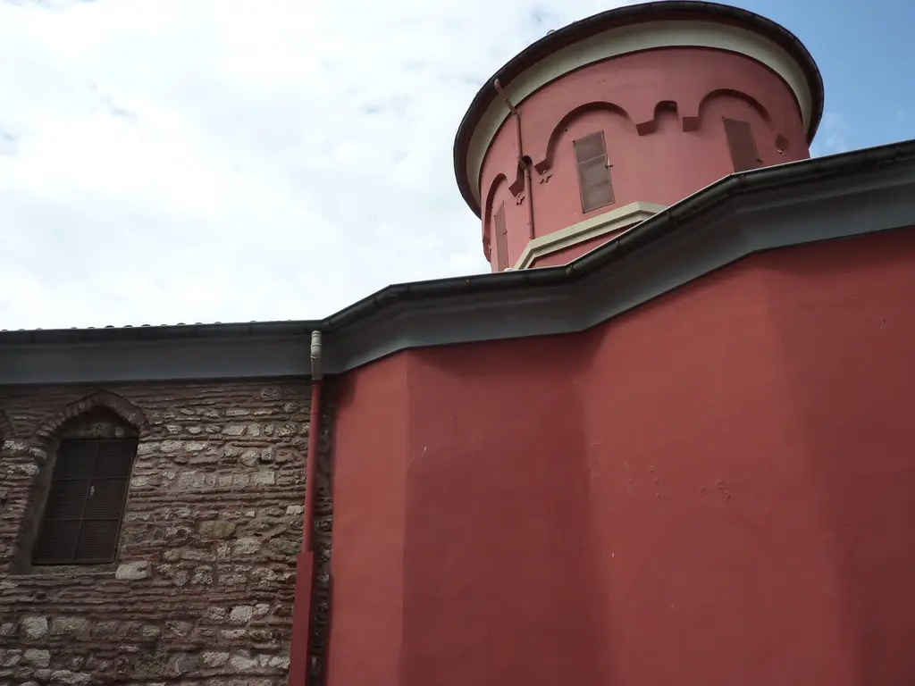 Kanlı Kilise'nin kubbe kulesi yakından; kırmızı sıvalı kasnak, kemerli pencereler, silme ve altında taş duvarlı yan cephe.