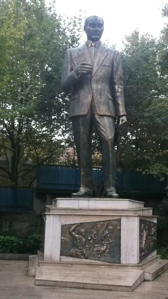 Maçka Demokrasi Parkı'nda takım elbiseli ayakta bronz Atatürk heykeli; mermer kaidede Kurtuluş Savaşı sahneli kabartma ve arkada ağaçlar.