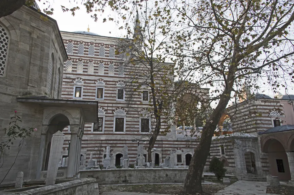Zal Mahmud Paşa Külliyesi'nin alt bahçesi; solda türbe duvarı, ortada caminin pencereli cephesi, kemerli giriş ve yaprakları dökülen çınar.
