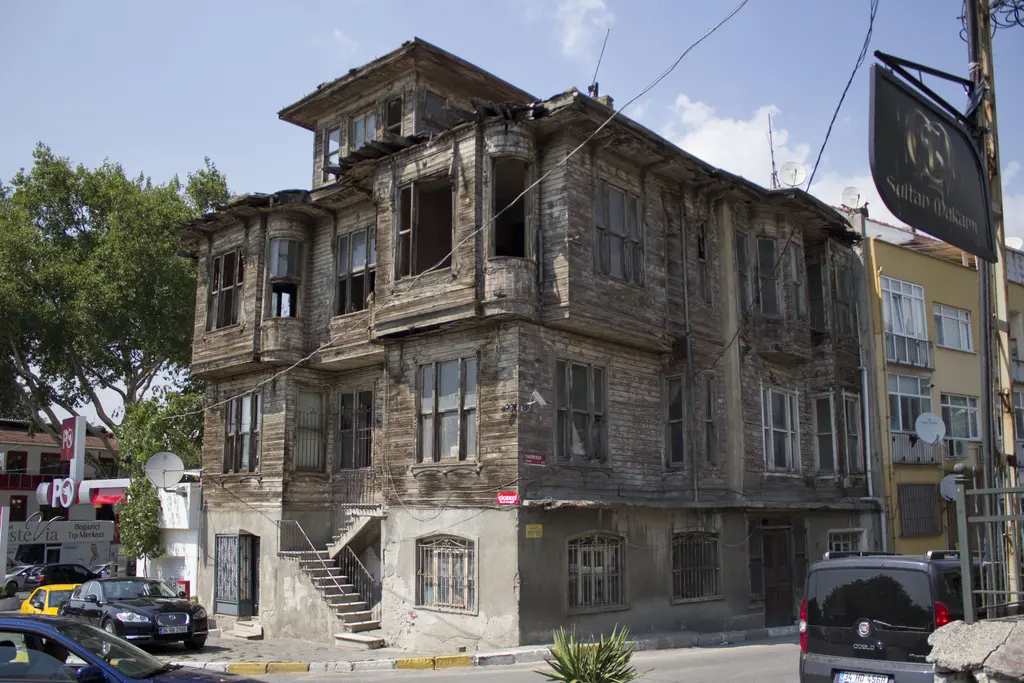 Çengelköy'de boyasız ahşap konak; üç katlı cephe, çıkmalar, kırık pencereler ve köşede taş merdiven.