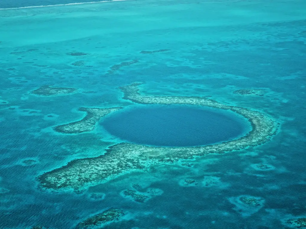 Belize'de Büyük Mavi Delik'in kuş bakışı görünümü; turkuaz sığlıklarla çevrili, mercan halkasının ortasındaki lacivert dev deniz obruğu.