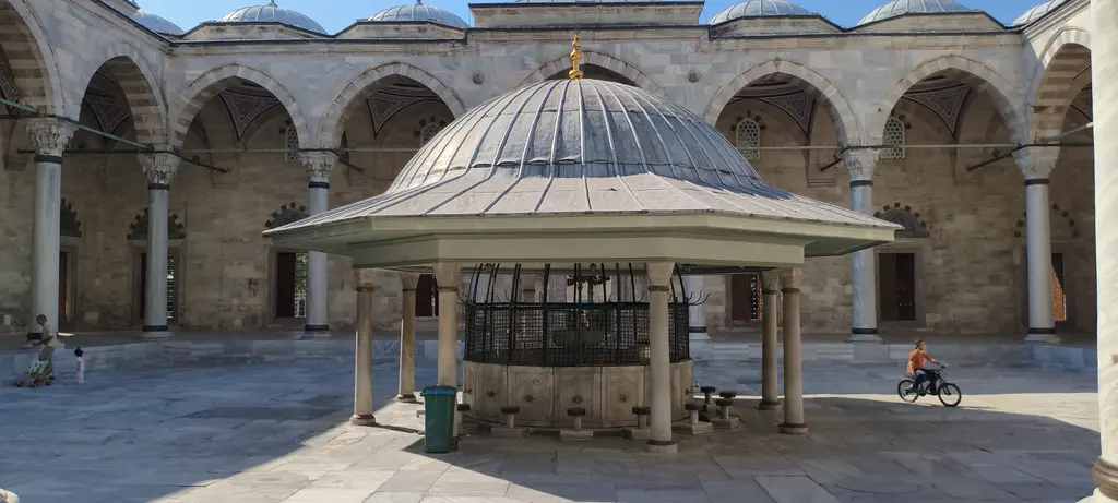 Yavuz Sultan Selim Camii'nin şadırvanı; sütunlara oturan çokgen kurşun çatı, arkada revak kemerleri ve sağda bisikletiyle geçen biri.