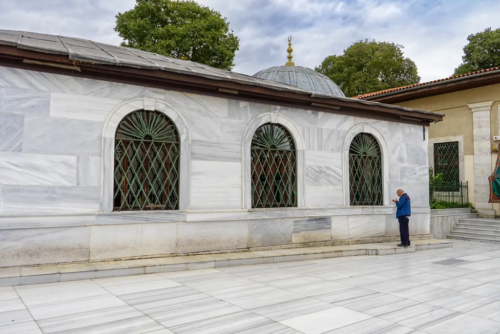 Merkez Efendi Türbesi'nin batı cephesi; baştan aşağı mermer kaplama, üç kemerli pencere, geniş ahşap saçak ve önünde taş döşeli meydan.