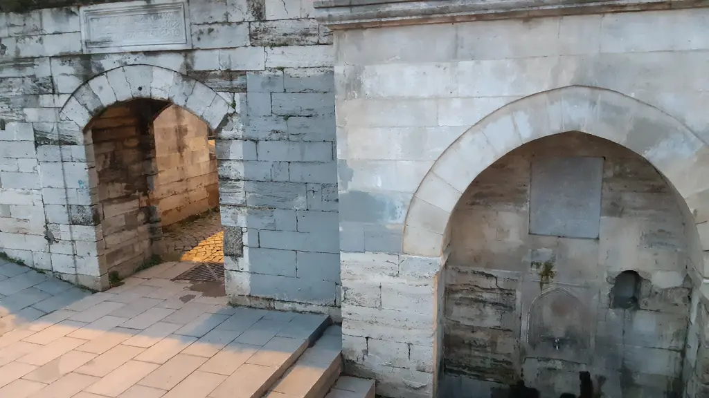 Defterdar Camii'nin cadde duvarı; kemerli avlu kapısı, yanında sivri kemerli taş çeşme ve önünde taş kaplı kaldırım.