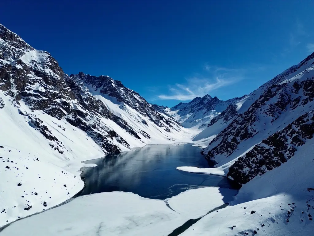 Portillo'da Laguna del Inca; karla kaplı dik yamaçların arasına sıkışmış koyu renkli dağ gölü ve masmavi gökyüzü.
