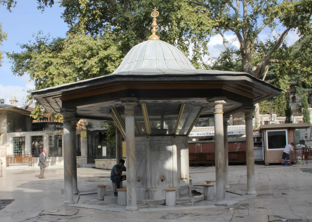Eyüp Sultan Camii'nin şadırvanı; kurşun külahlı saçak, mermer sütunlar, abdest muslukları ve arkada çınarlar.