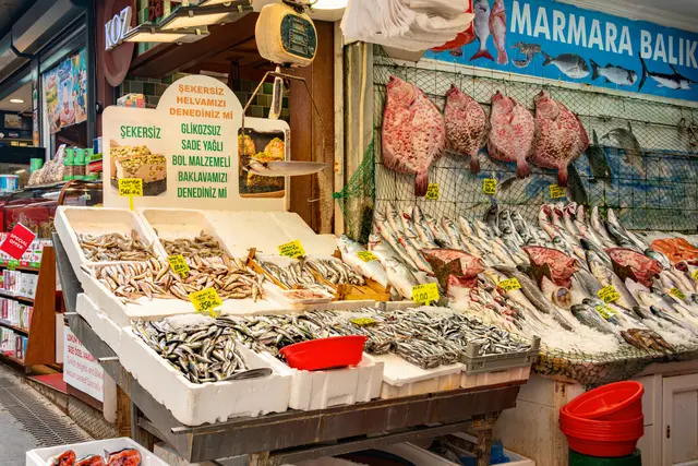 Kadıköy Çarşısı'nda balık tezgâhı; renkli tabelalar, buz üstünde balıklar, kasalar ve fiyat kartları.