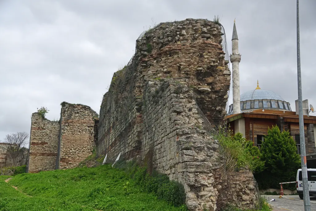 Edirnekapı'da Theodosius surlarının yıkık bir bölümü; taş ile tuğla örgülü burç kalıntısı, önünde çimenlik ve arkada caminin kubbesi ile minaresi.