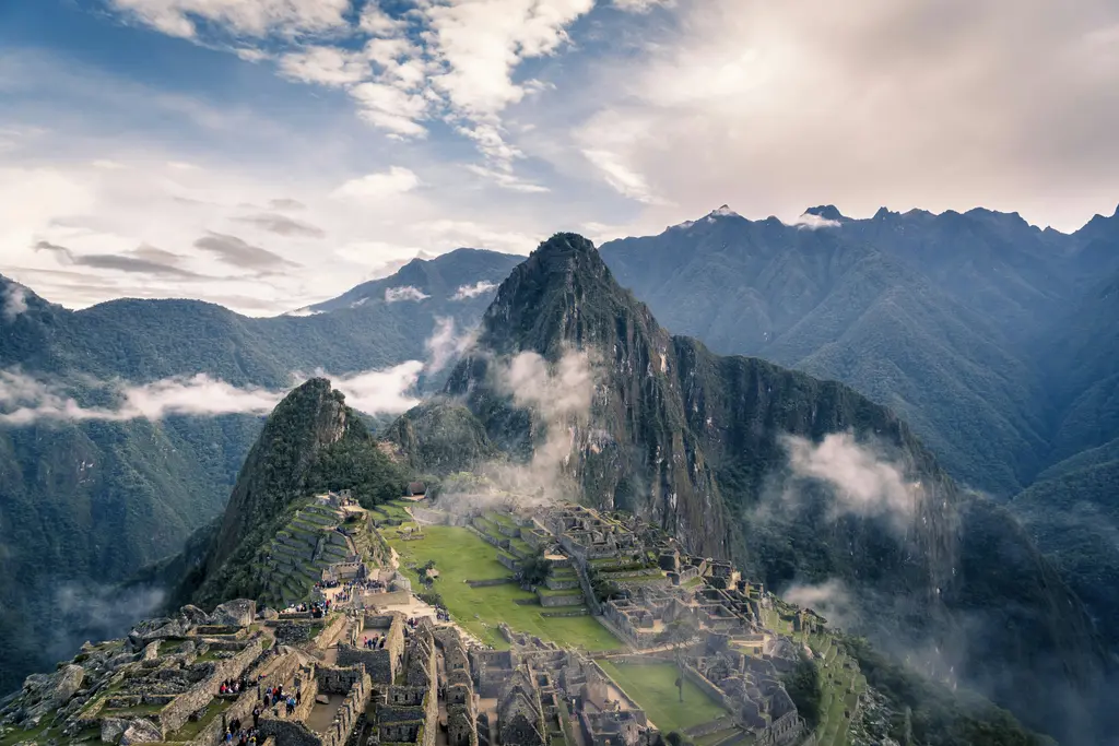 Peru'da And Dağları'nın sisli zirveleri arasındaki Machu Picchu İnka şehri; taş teraslar, yıkıntı yapılar ve arkada bulutlara karışan Huayna Picchu tepesi.