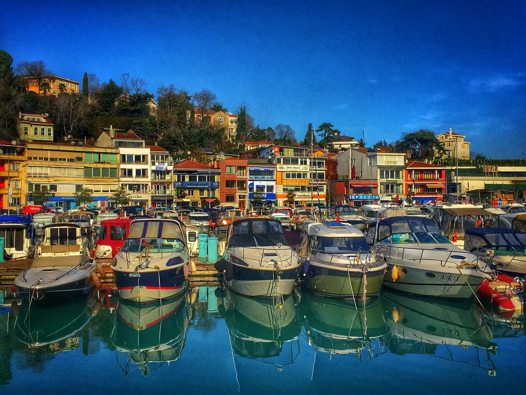 Tarabya'da marinada yan yana demirli tekneler; suya yansıyan gövdeler, arkada renkli cepheli binalar.